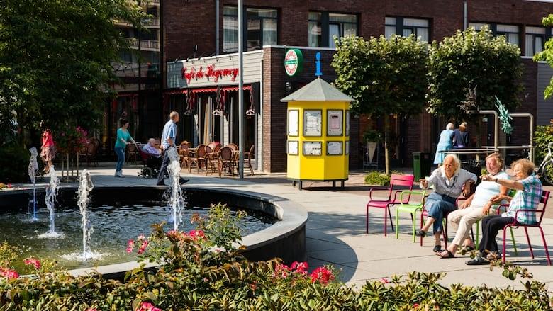 Leafy green street with people sitting around talking and a fountain.