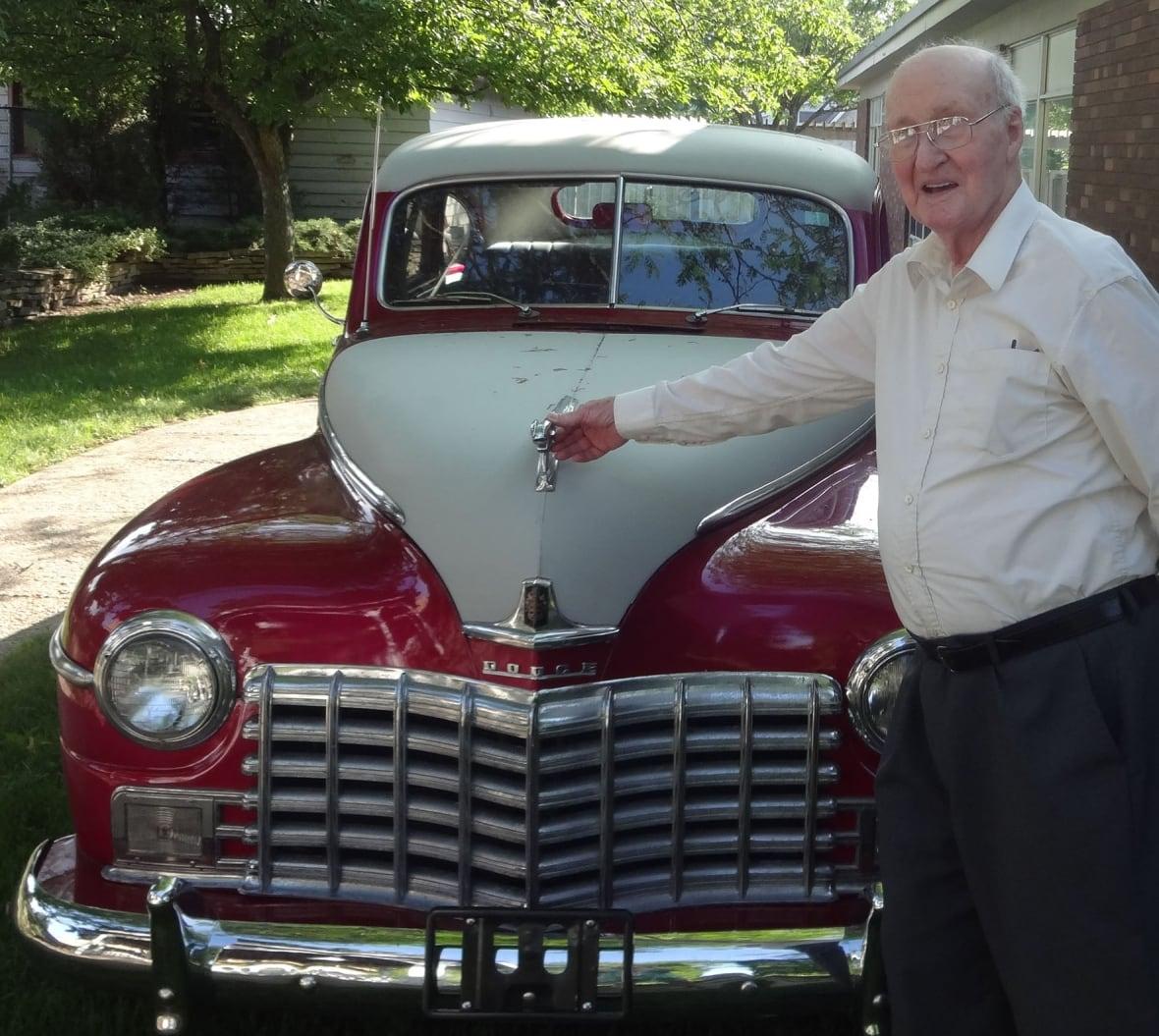 Elderly man posing with old school car.