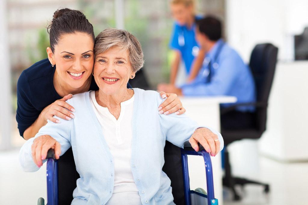Old lady in wheel chair smiling with nurse giving her a hug from behind